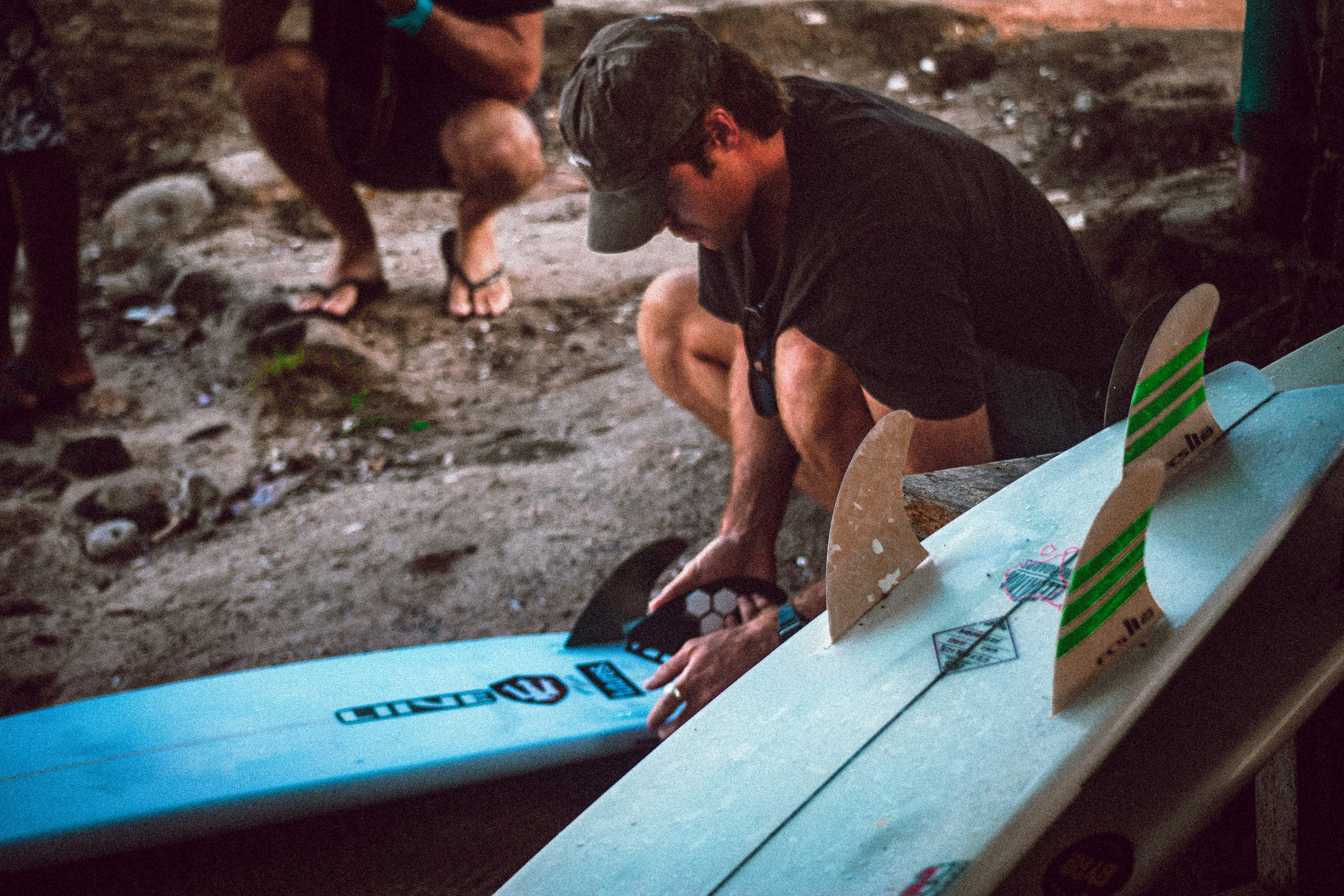 Un hombre arrodillado junto a una tabla de surf