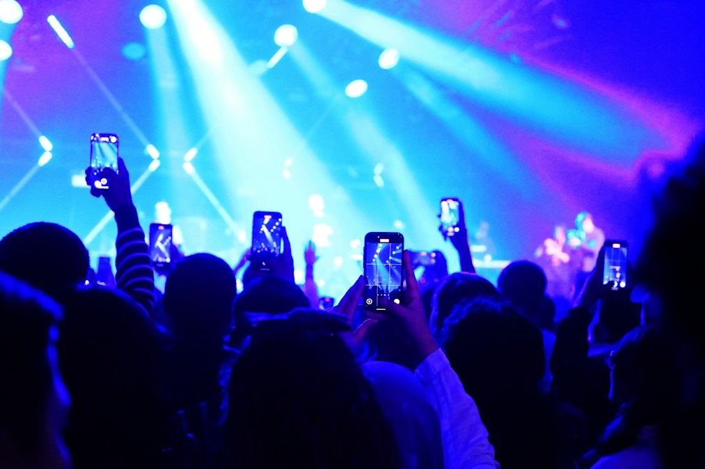 Public d’une salle de concert brandissant des smartphones sous les projecteurs bleus, une ambiance comparable à celle attendue à Forest National le 25 octobre 2026