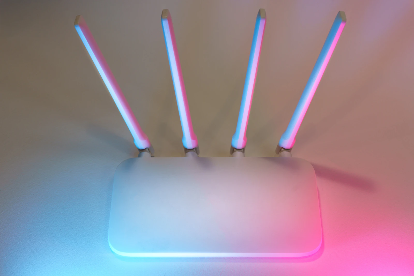 Close-up top-down view of a modern white wireless router with four antennas, illuminated by pink and blue light against a neutral background