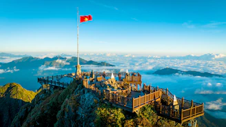 A flag on top of a mountain with clouds in the background