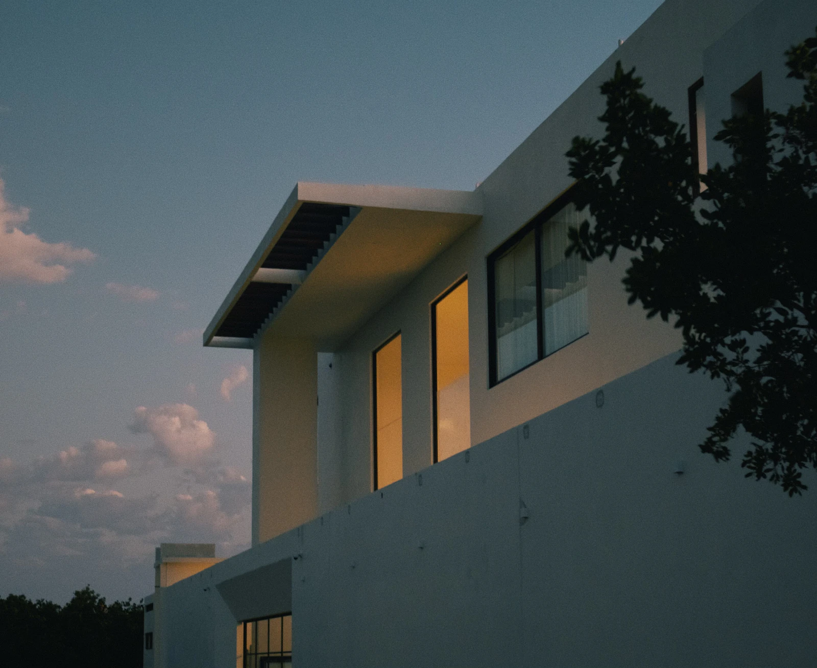 Fachada de casa moderna com as janelas fechadas ao fim da tarde.