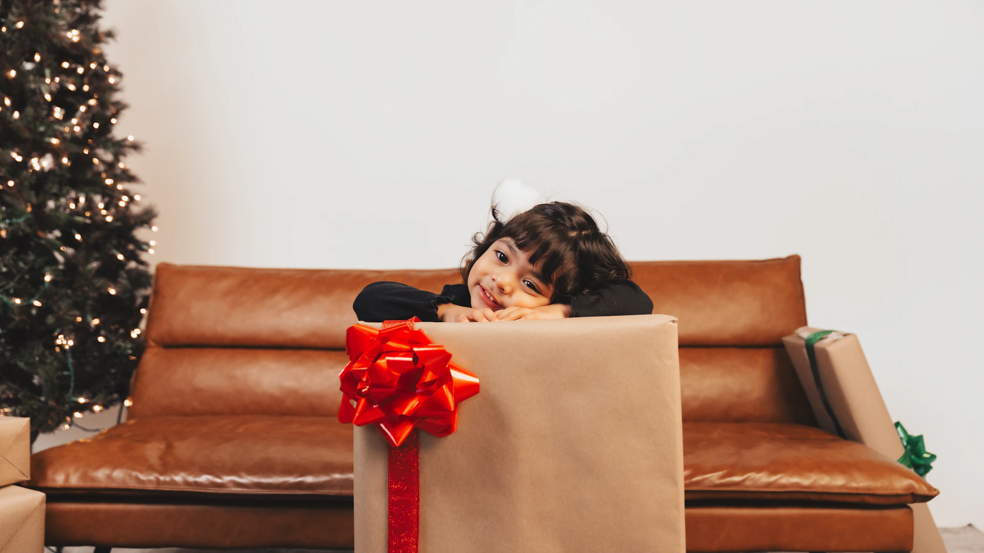 A little girl sitting on a couch with a christmas present in front of her