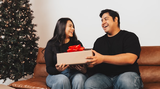 A man and woman sitting on a couch holding a box