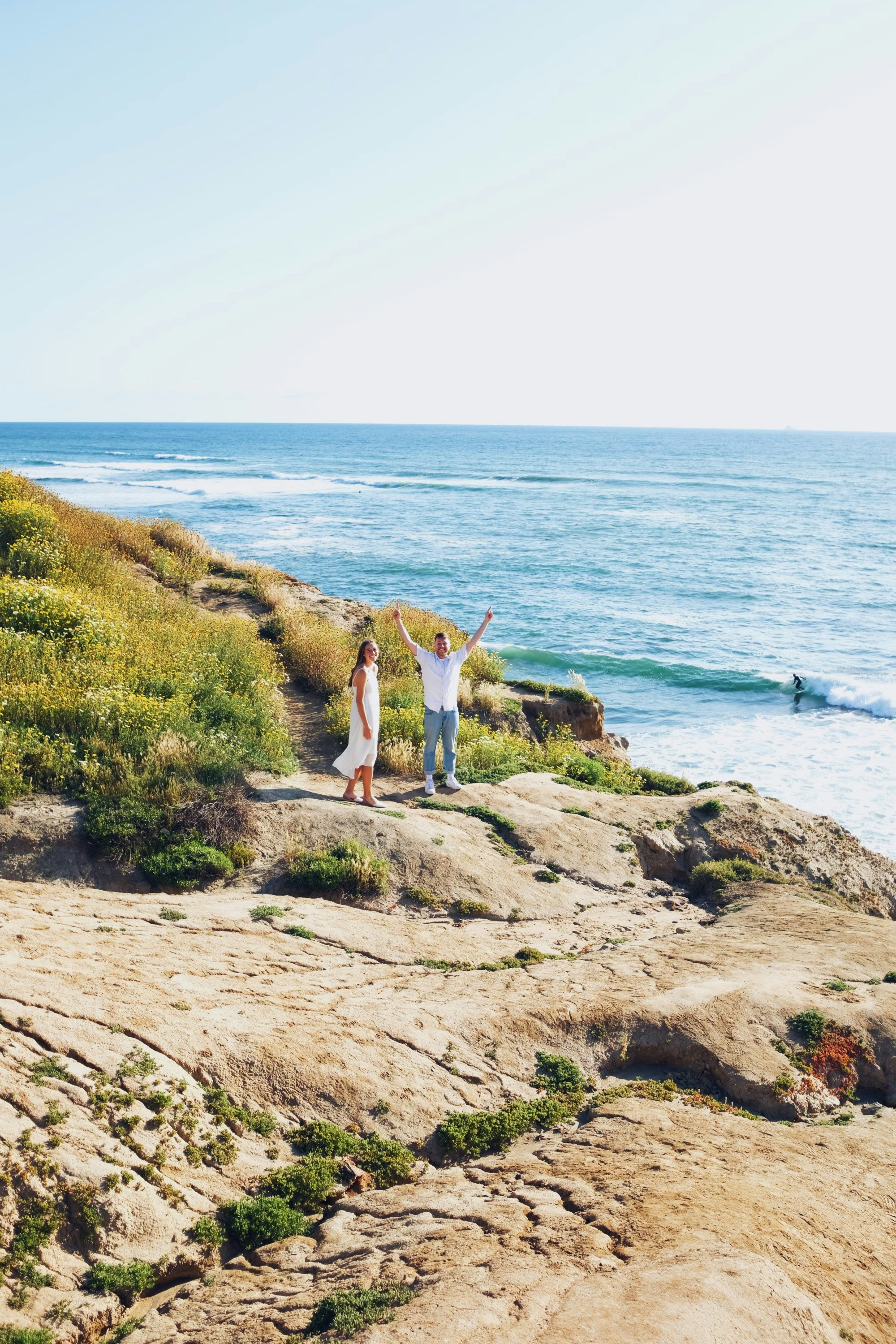 A couple of people standing on top of a cliff near the ocean