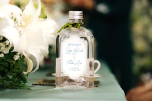 A bottle of alcohol sitting next to a bouquet of flowers