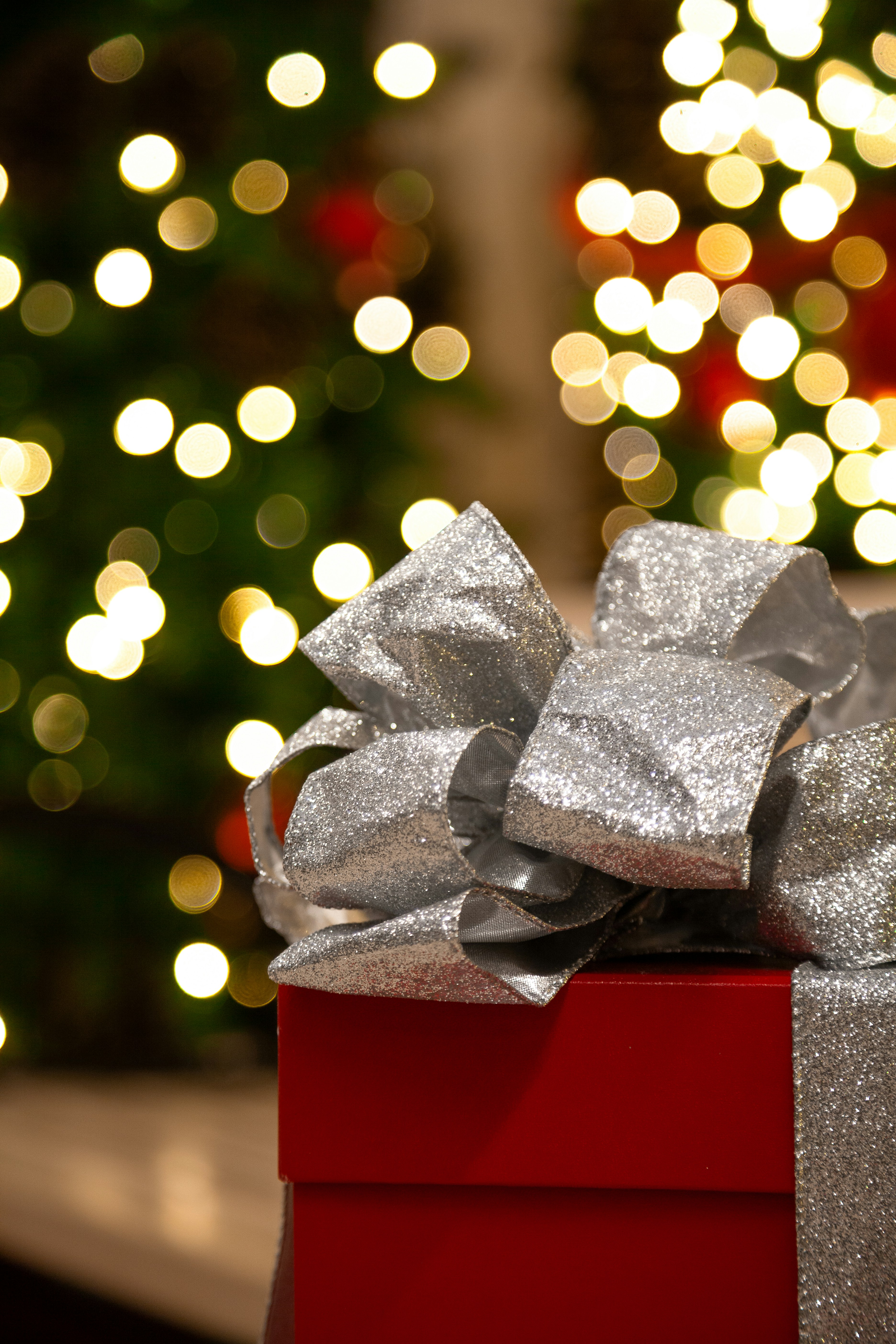 Eine rote Schachtel mit einer silbernen Schleife und einem Weihnachtsbaum  im Hintergrund Foto – Kostenloses Bild zum Thema Weihnachten auf Unsplash, image size:3000x4500