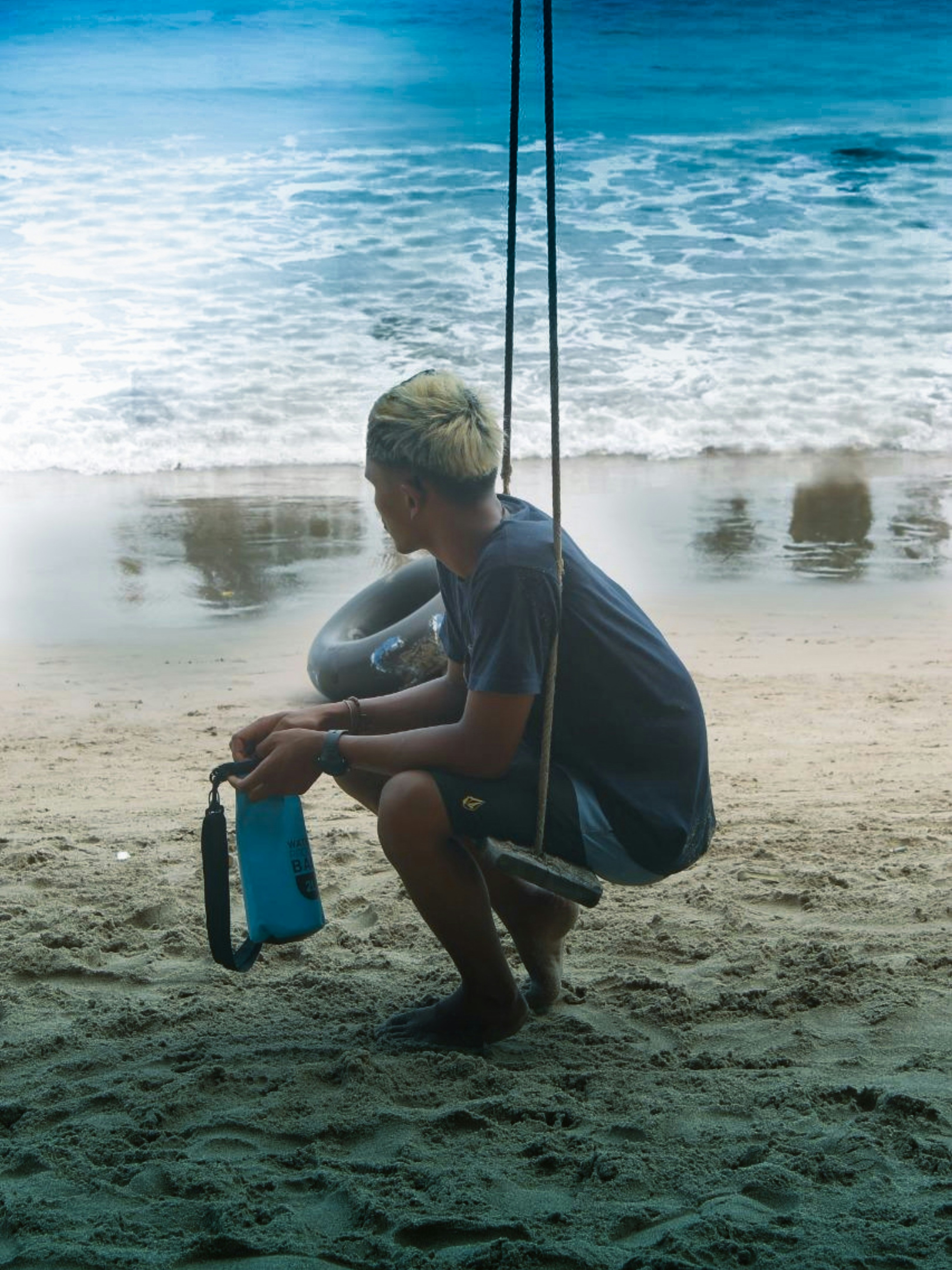 Seorang anak laki-laki duduk di ayunan di pantai