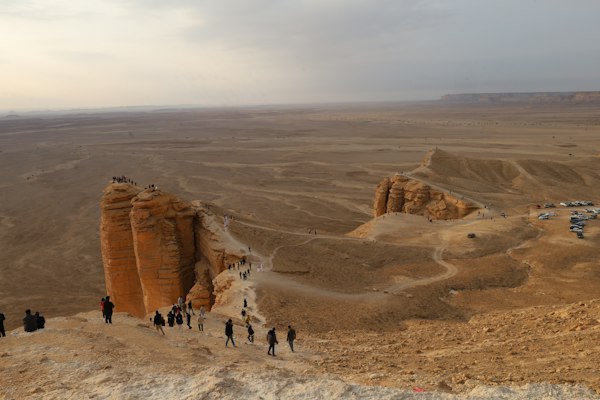 بازدیدکنندگان بر لبه‌ی صخره‌های بیابانی مشرف به دشت