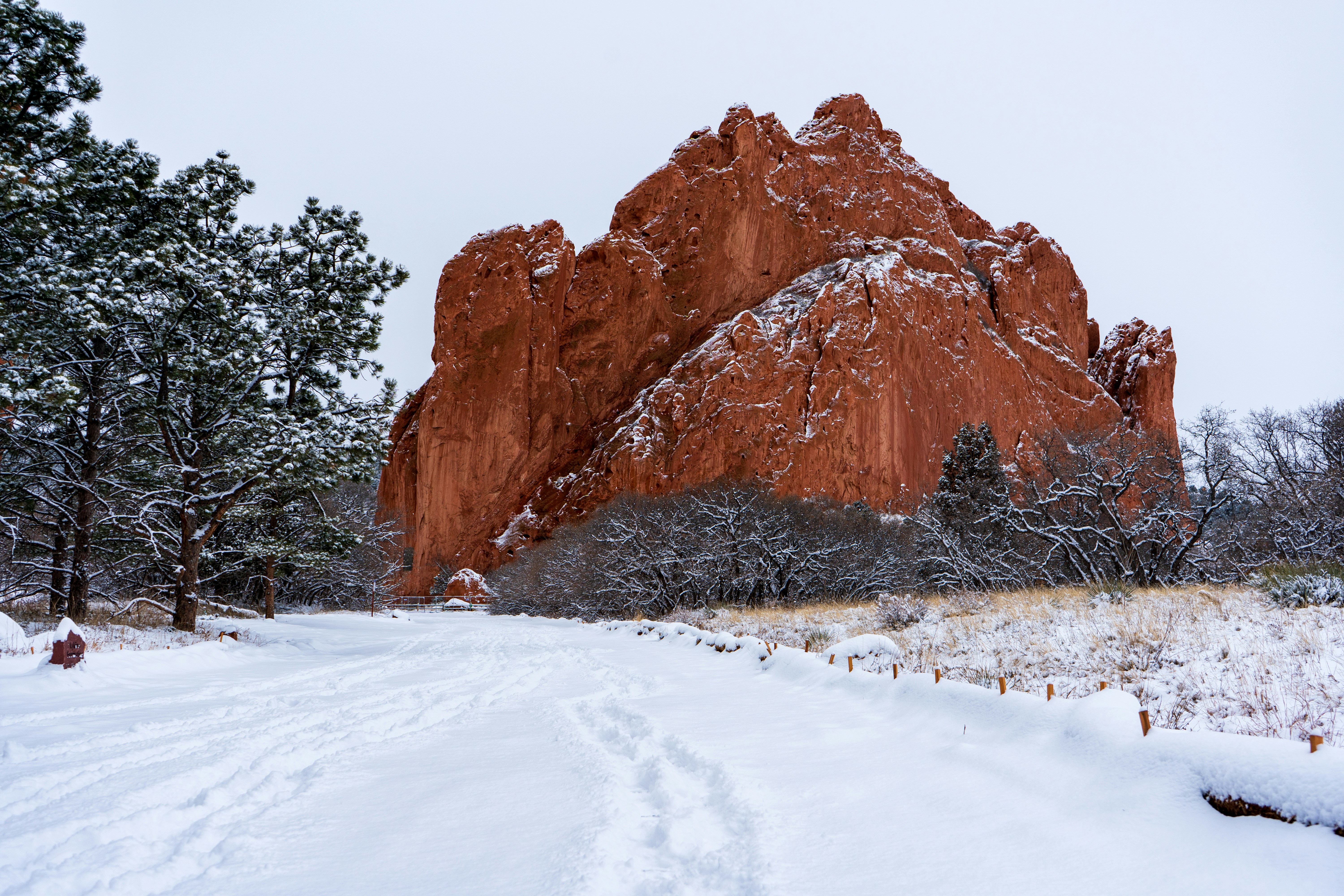 A snow covered road in front of a large rock formation