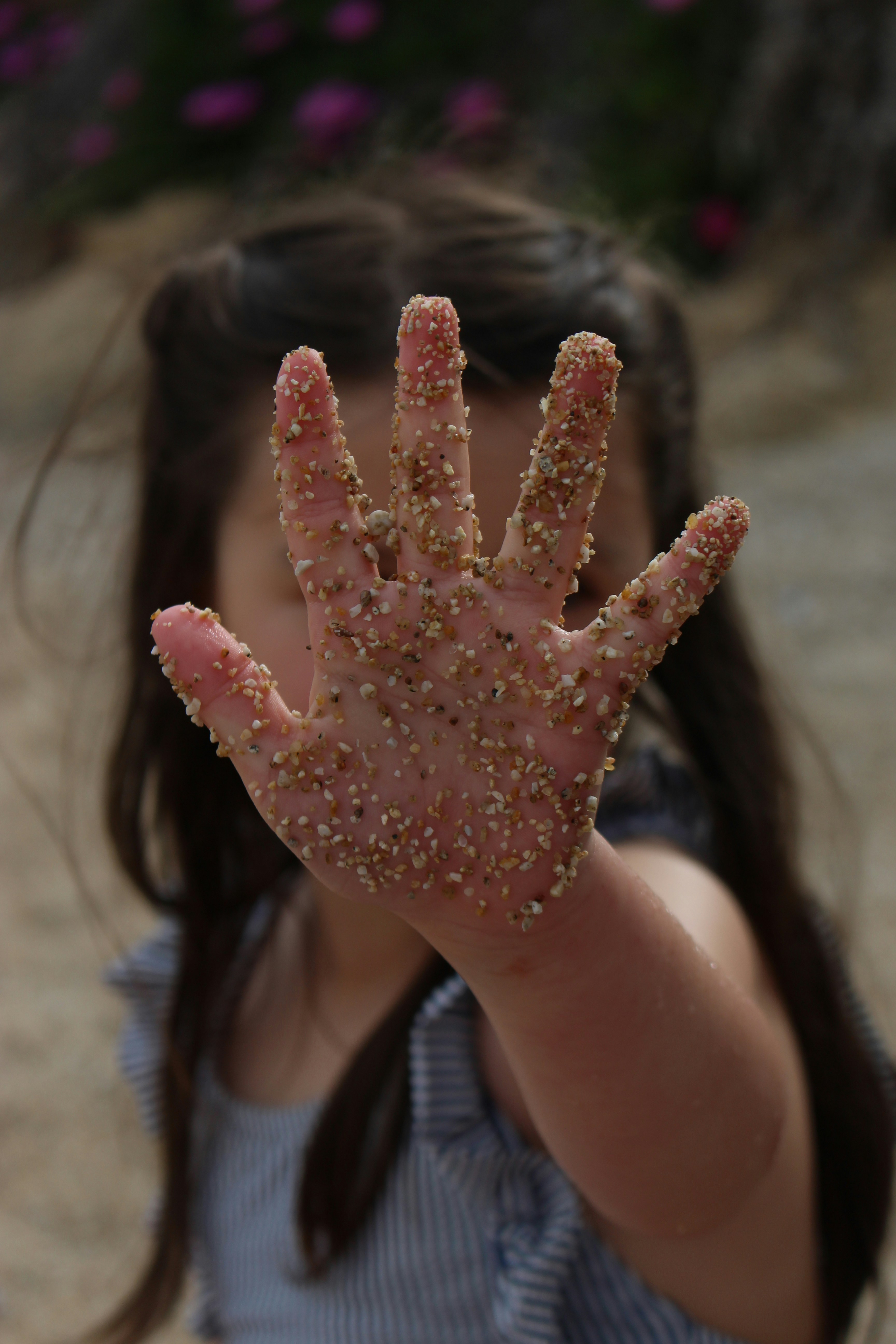 A young girl holding up her hand covered in sand