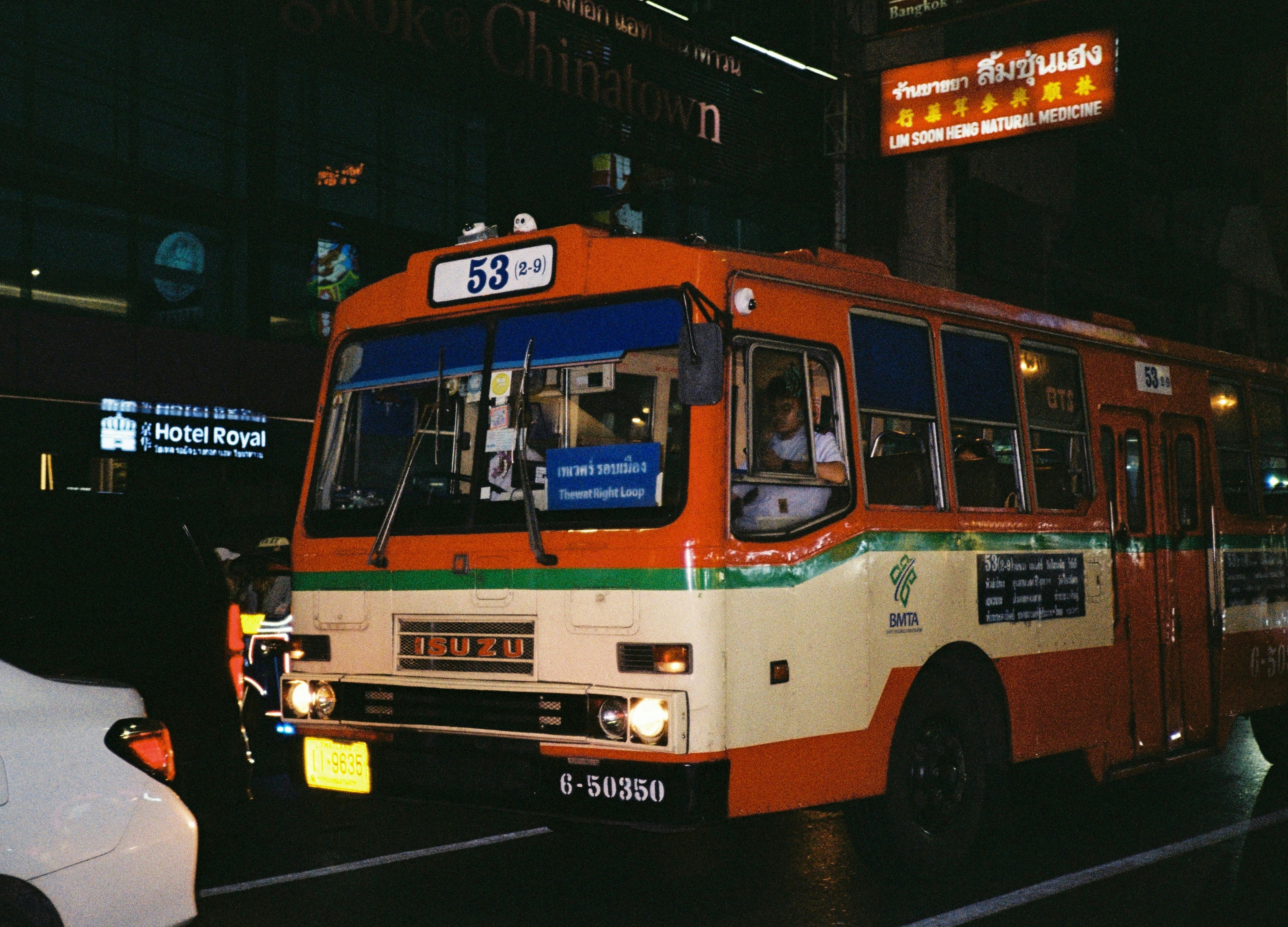 An orange and white bus driving down a street at night