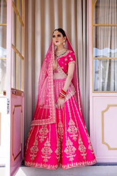 A woman in a pink lehenga standing in front of a doorway