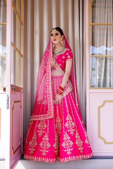 A woman in a pink lehenga standing in front of a doorway