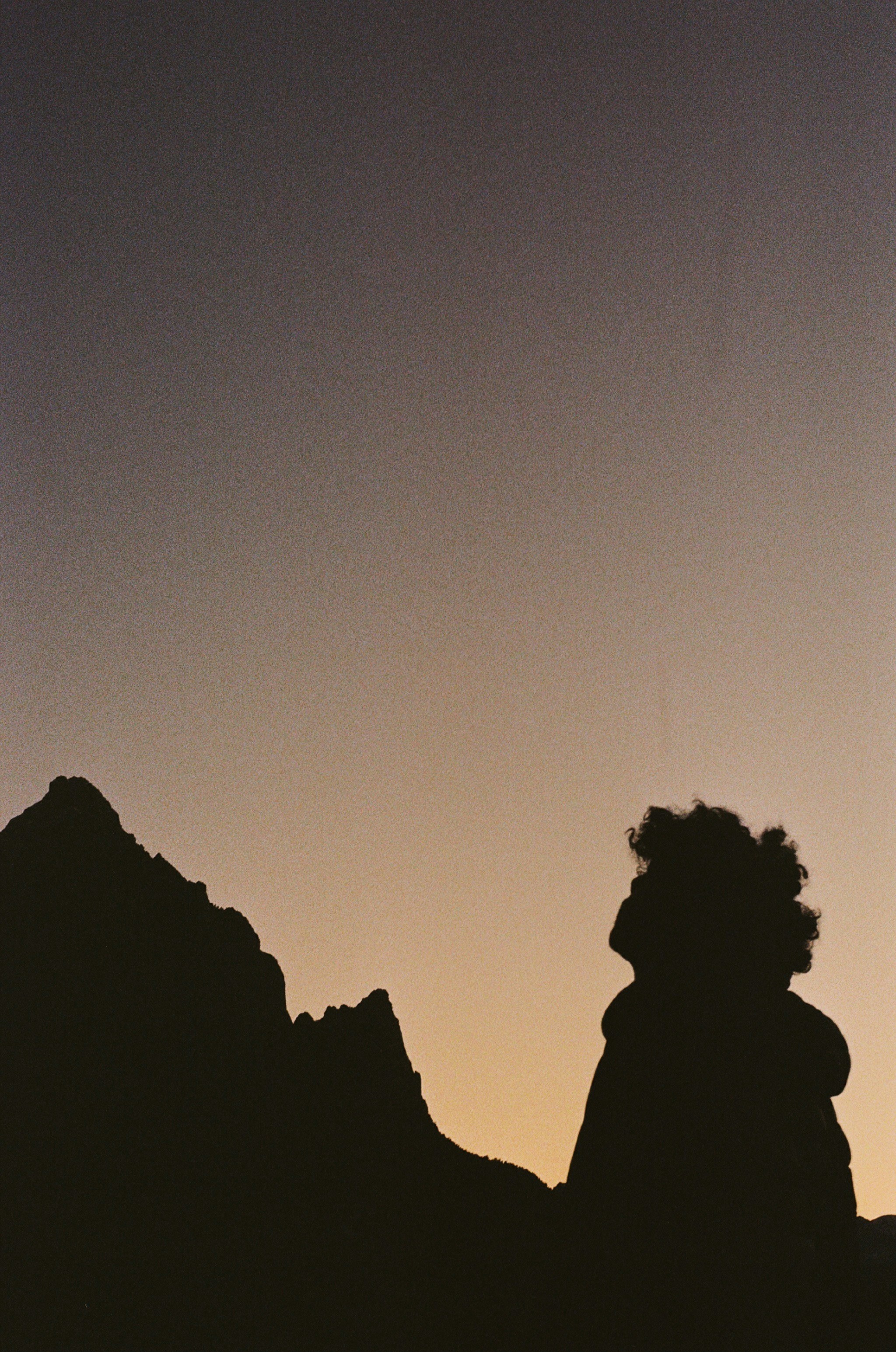 A silhouette of a person sitting on top of a mountain