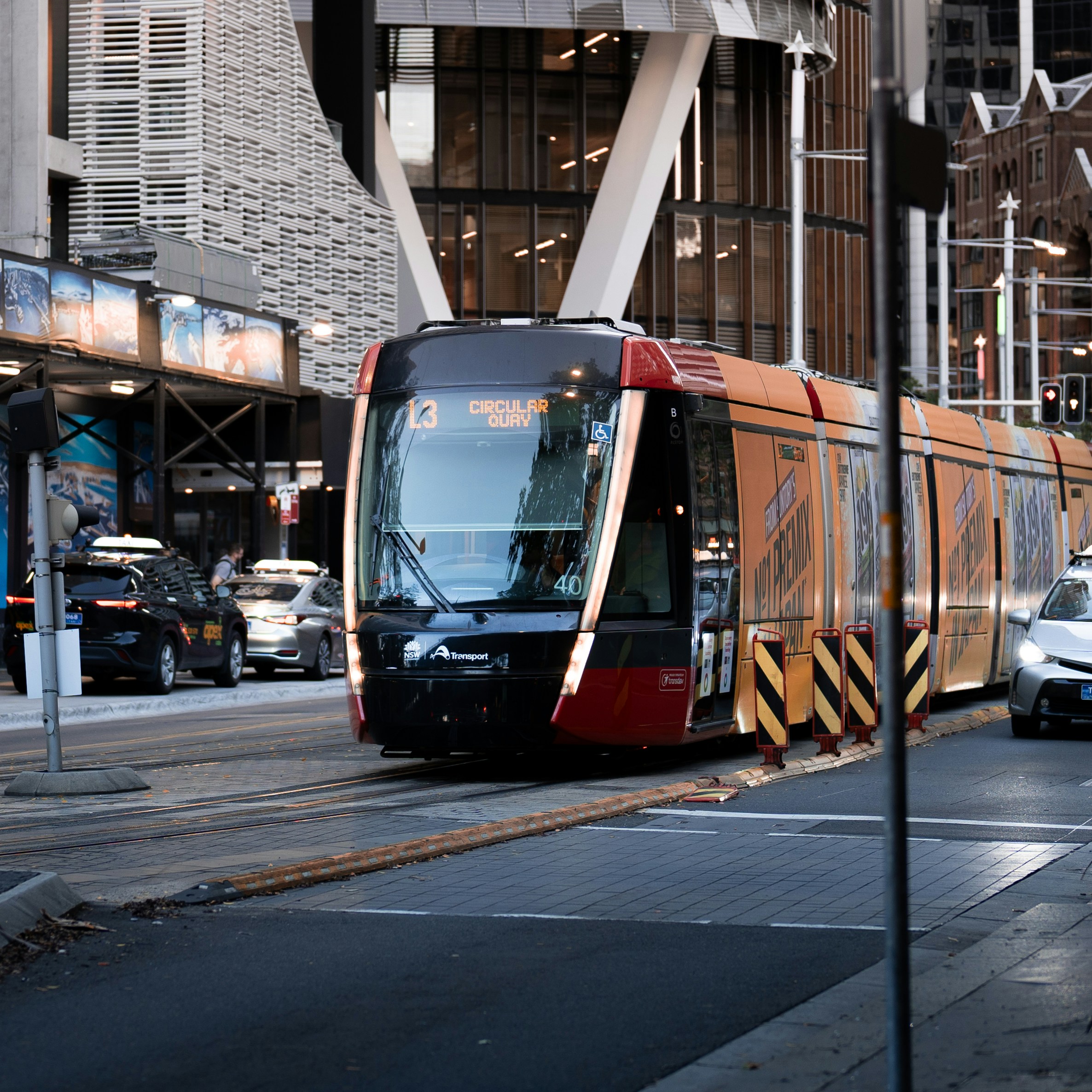 Un tren rojo y naranja que viaja por una calle junto a edificios altos