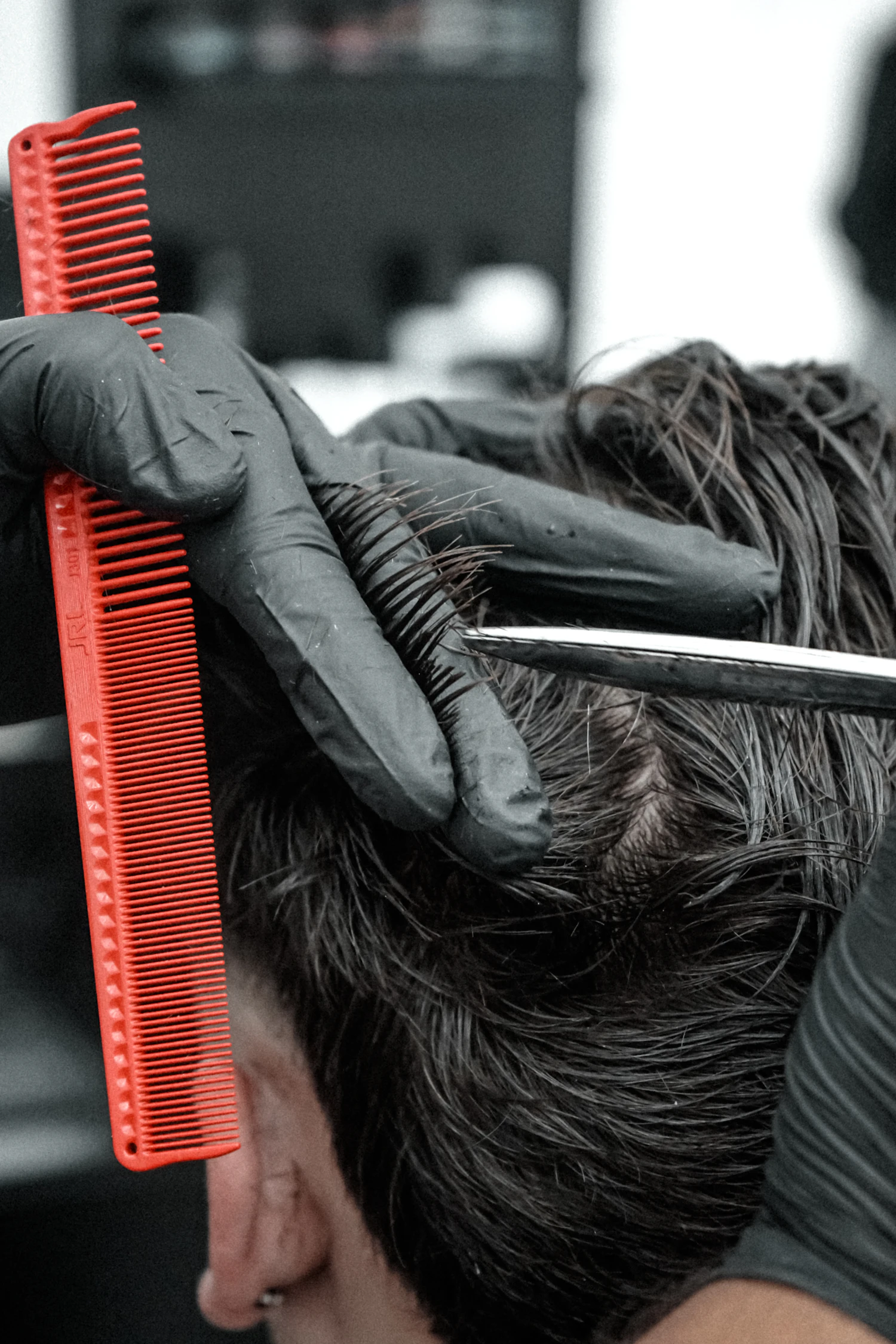 A red comb lifting grey hair while a straight blade follows it across the top of a head