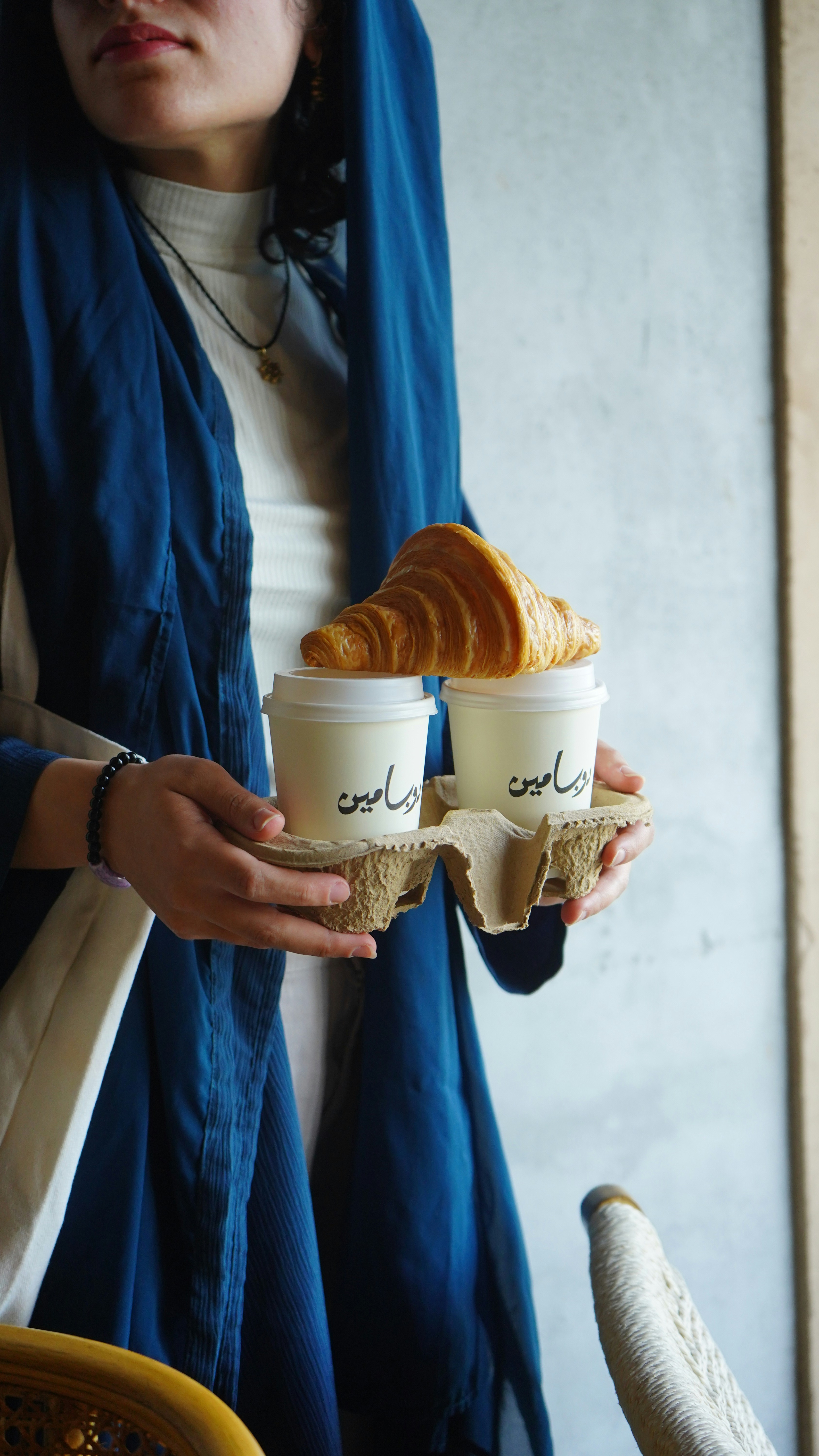 A woman holding two cups of coffee with croissants in them