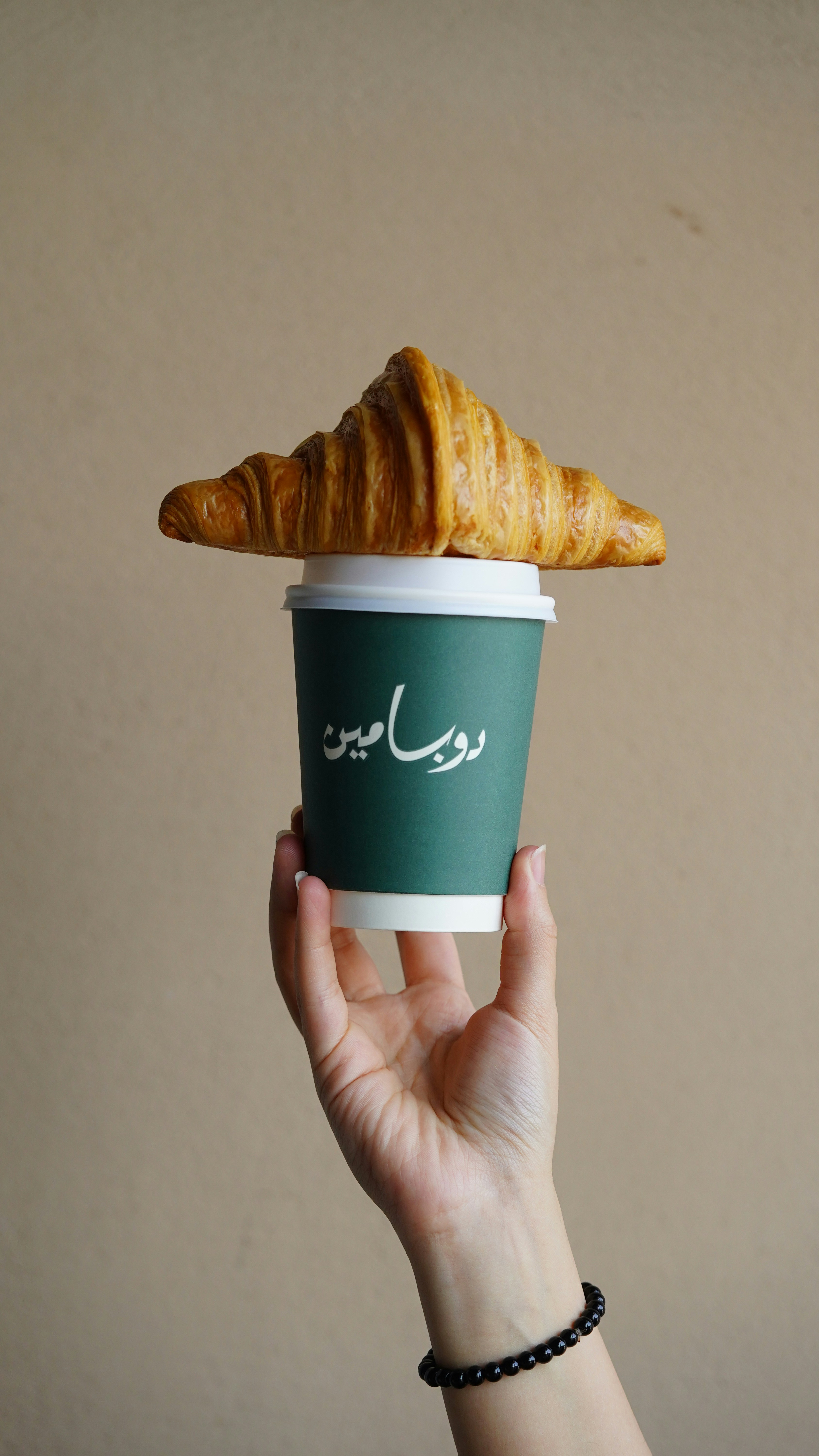 A person holding a cup of coffee with a croissant on top of it