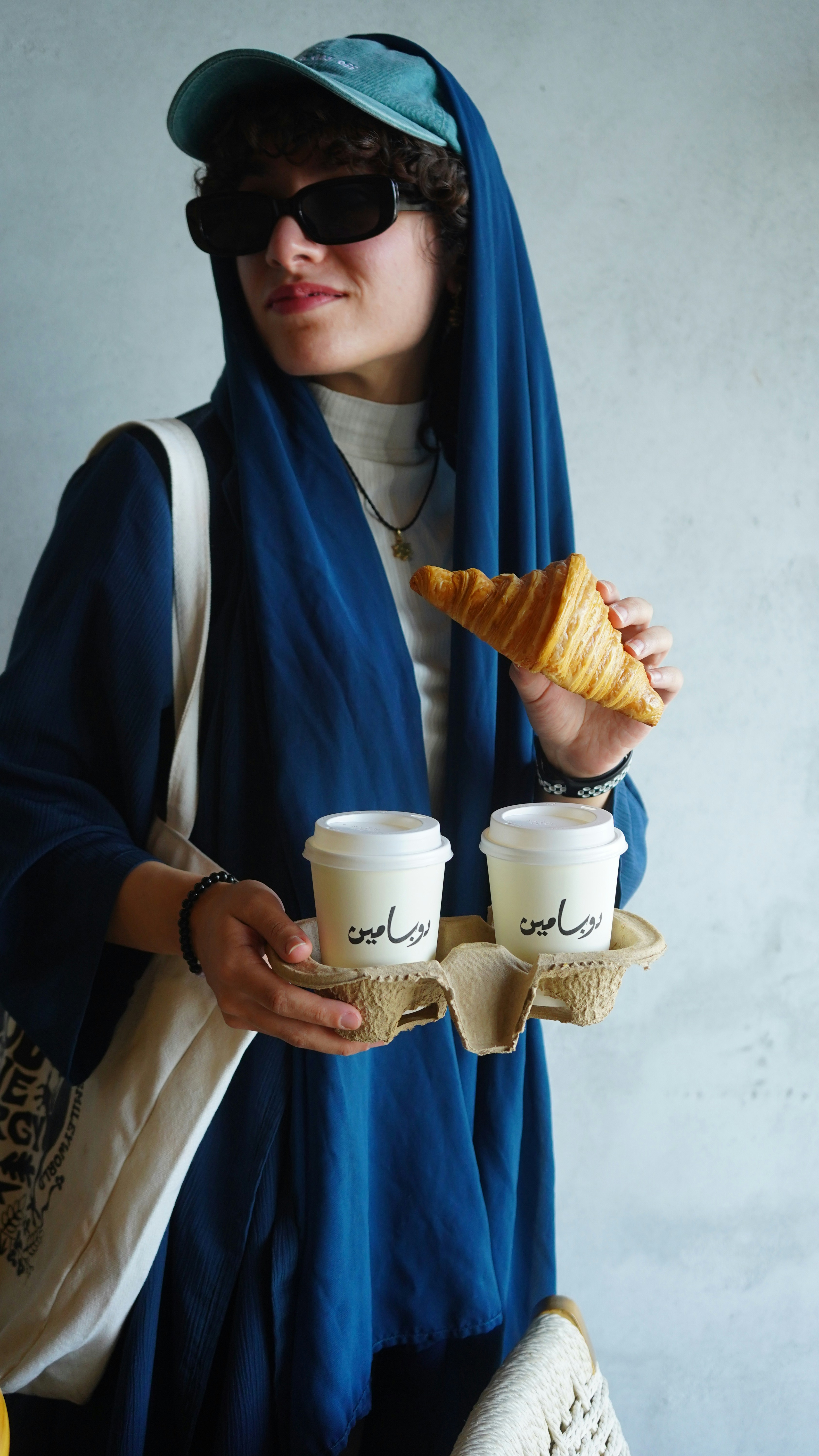 A woman holding two cups of coffee and a croissant