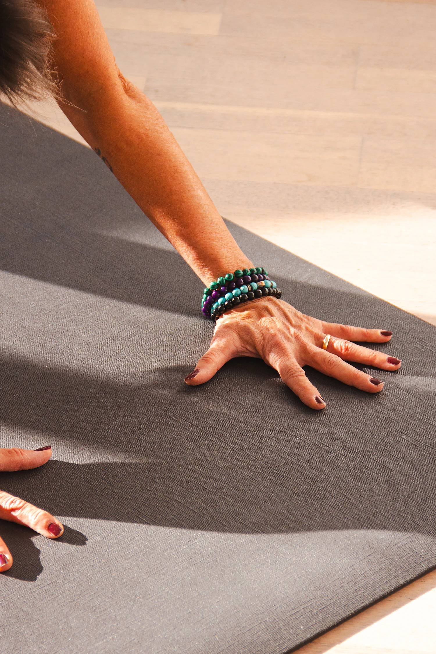 A hand with stacked bracelets planted flat on a grey mat, warm floor beyond it