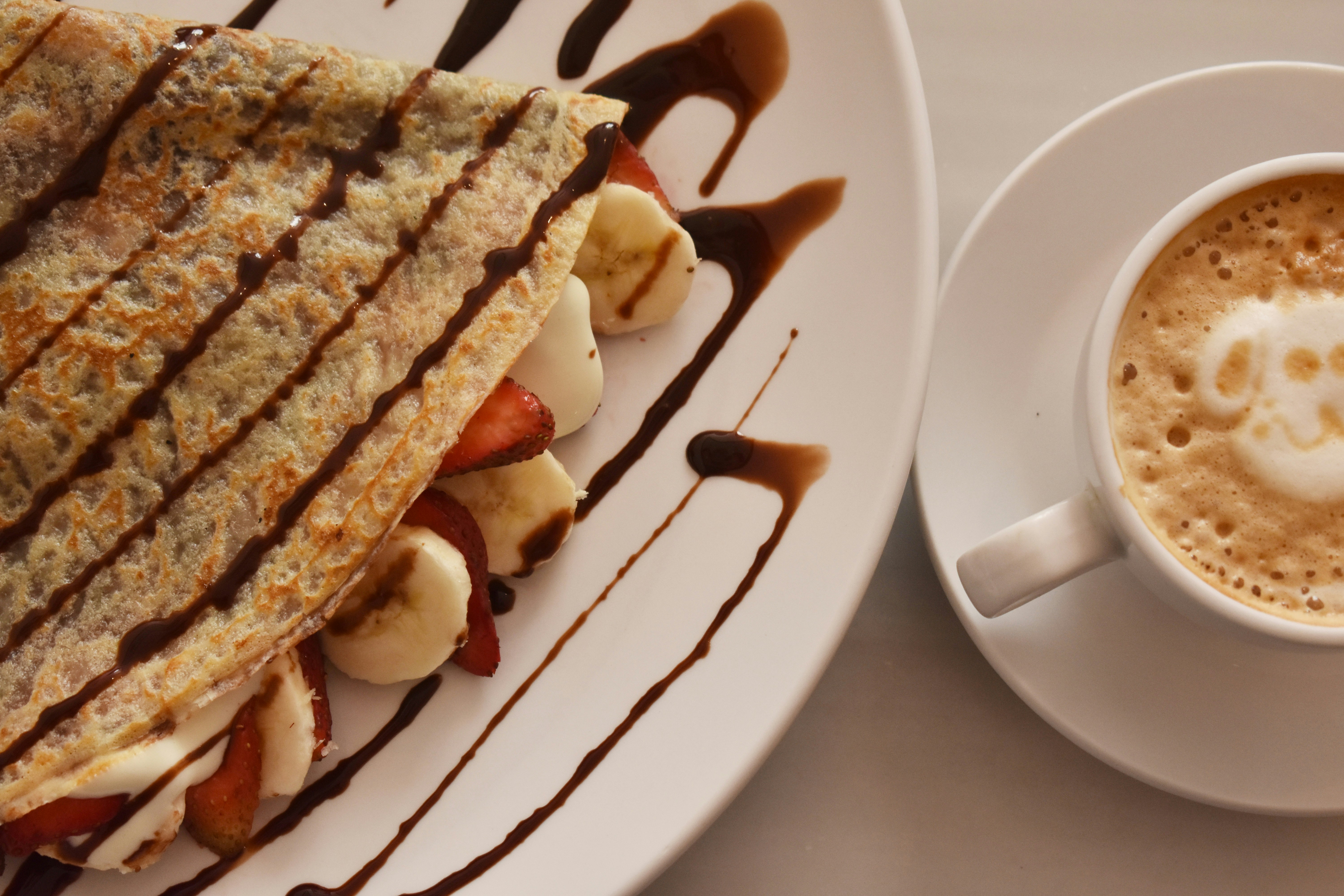 A white plate topped with a cut in half sandwich next to a cup of coffee