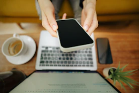 A person holding a cell phone over a laptop