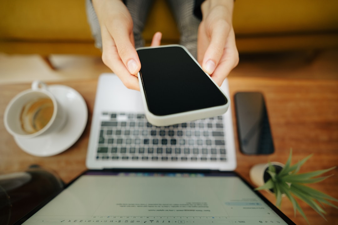 A person holding a cell phone over a laptop