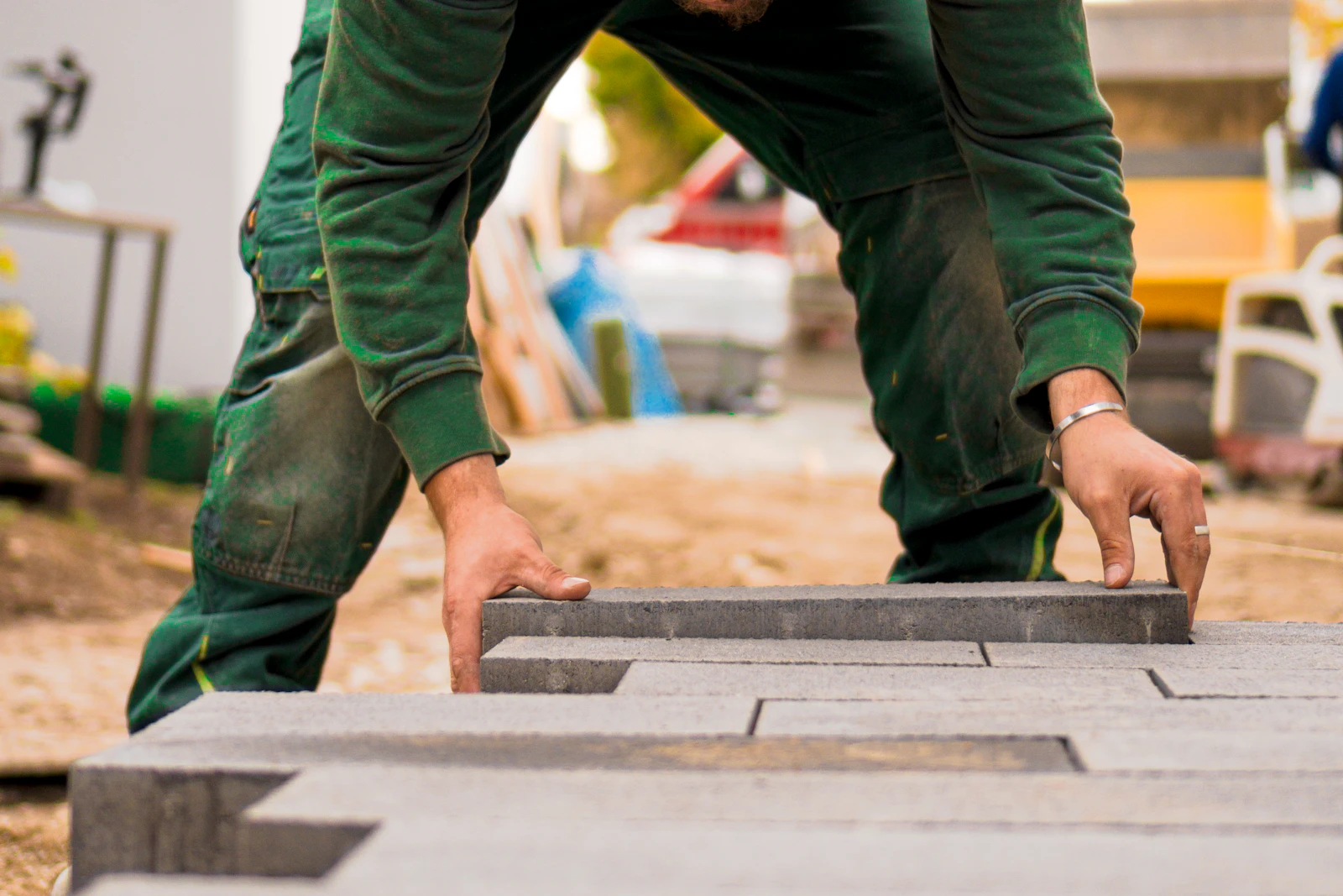 Hände eines Pflasterers beim Verlegen großformatiger Betonsteinplatten im Splittbett