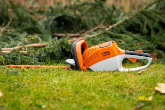 An orange and white chainsaw laying on the grass
