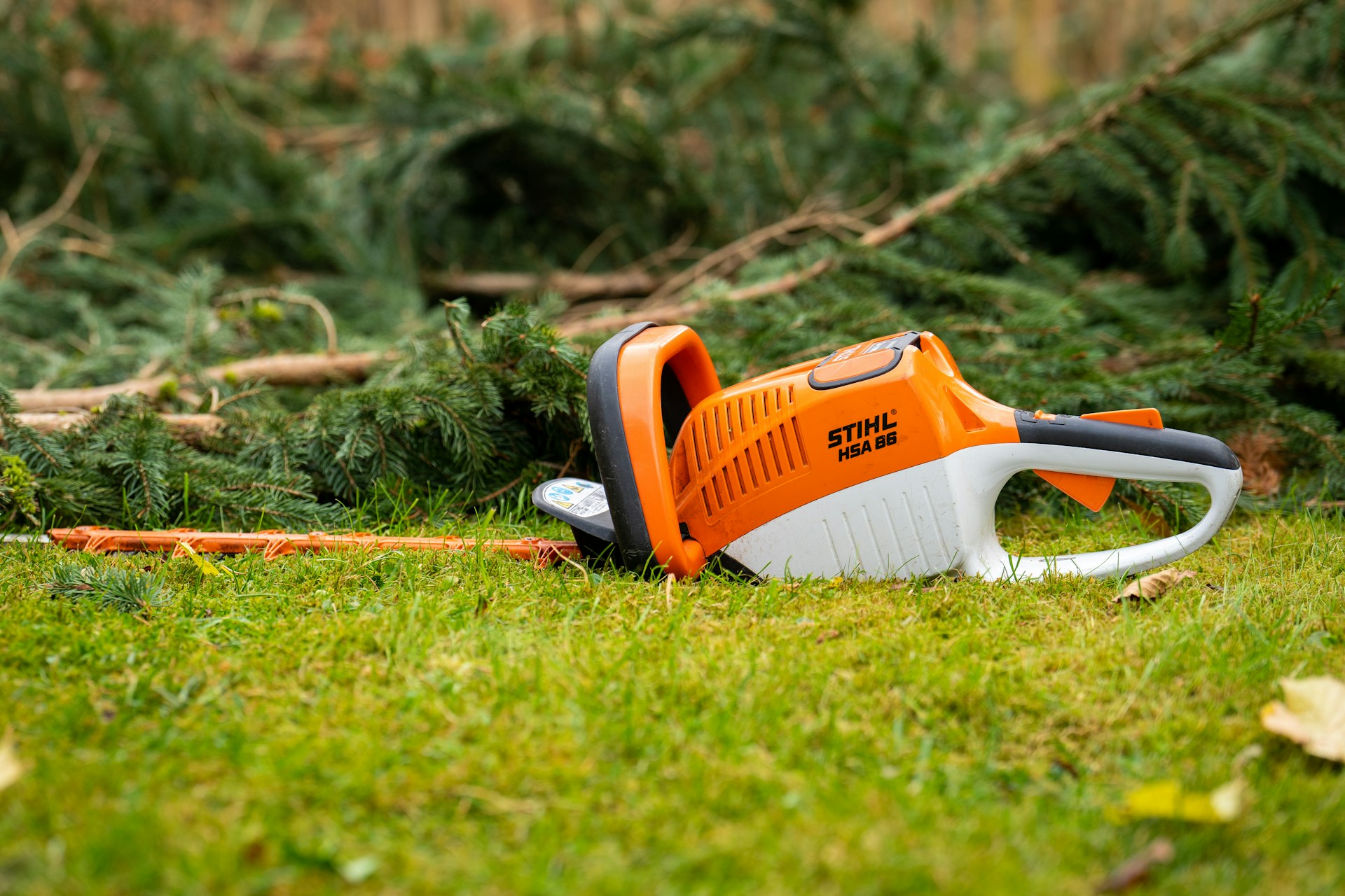 An orange and white chainsaw laying on the grass