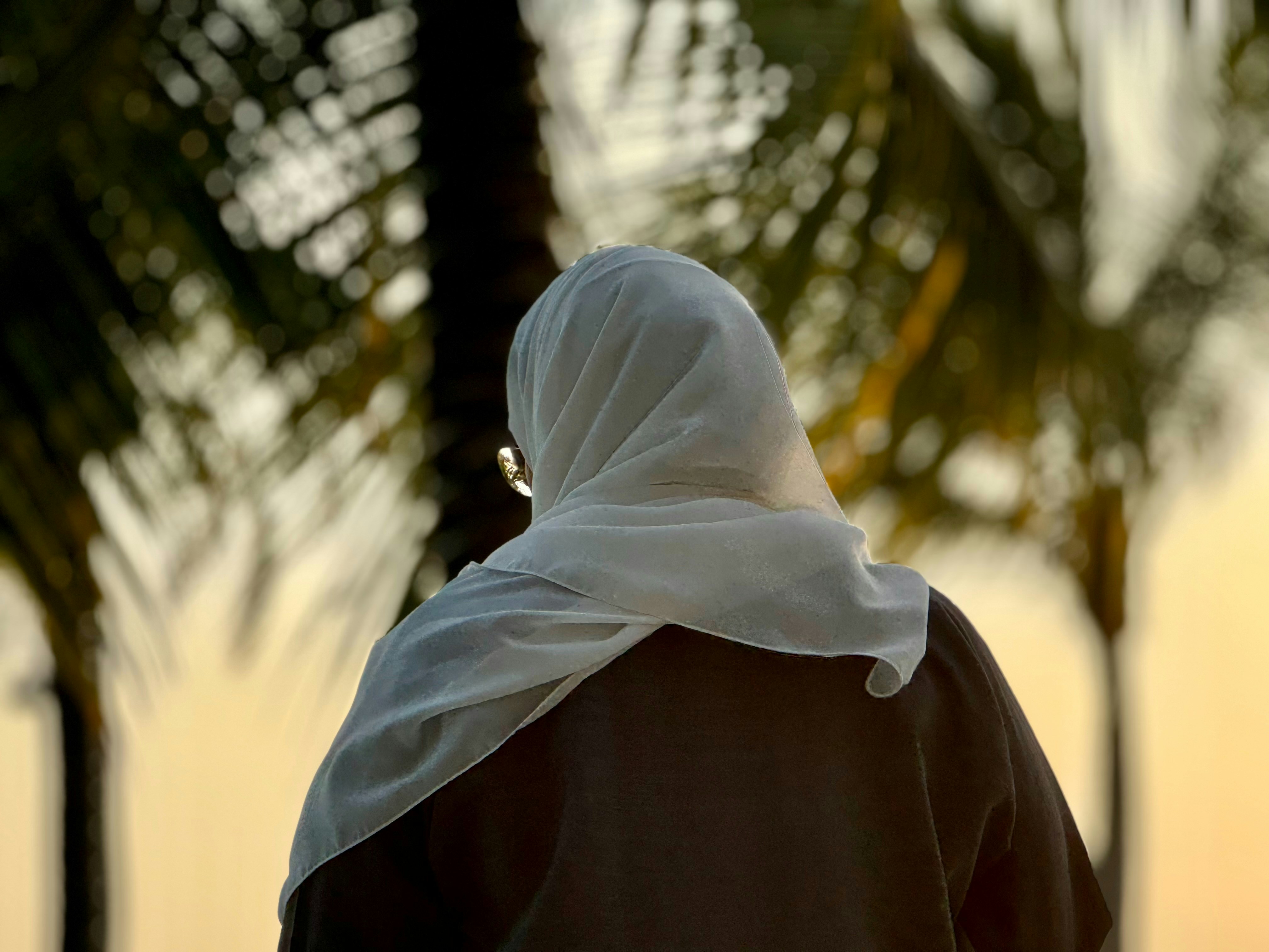 A woman walking down a street past palm trees