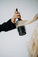 A hand using a round brush to style long blonde hair