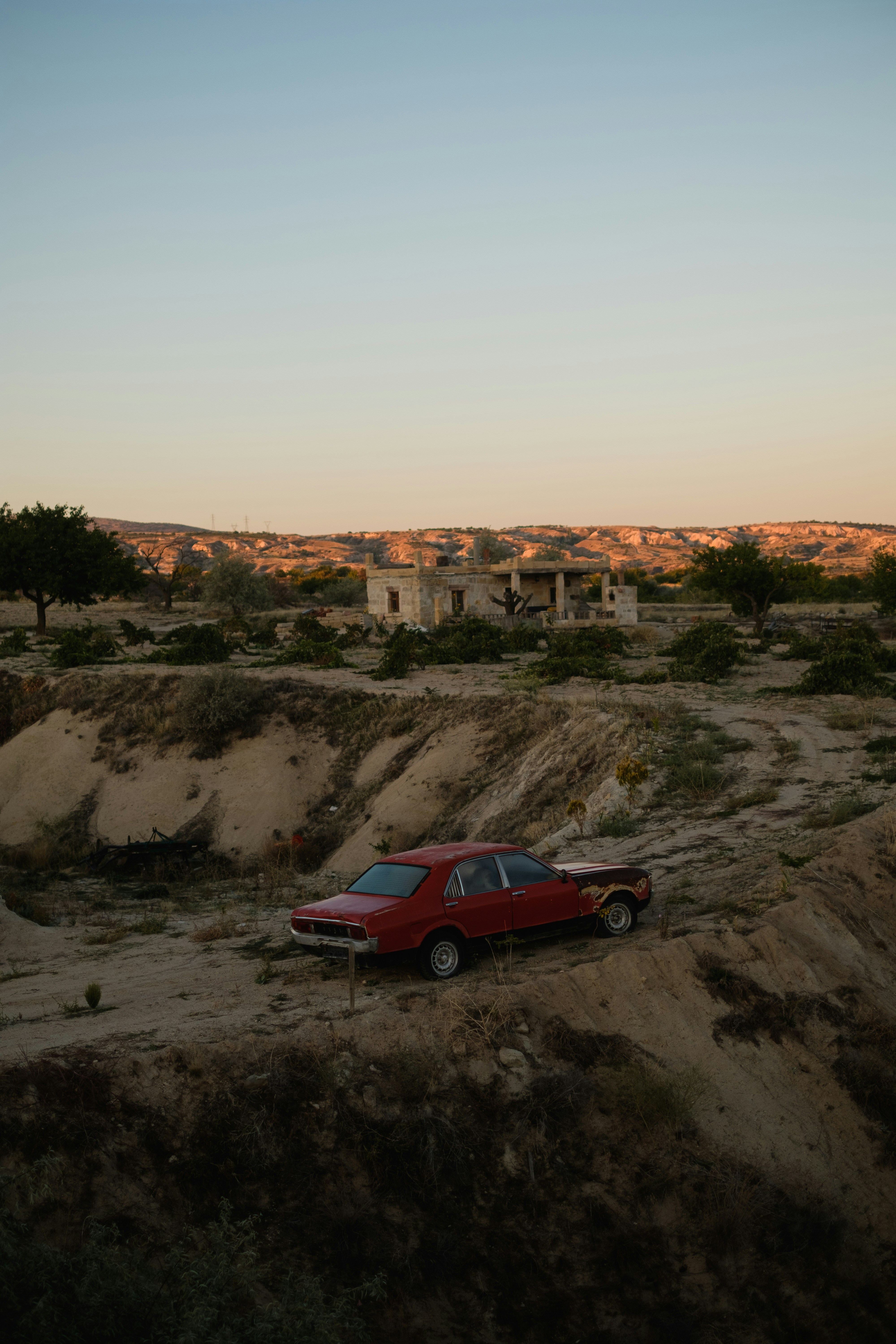 A red car is parked on a dirt road