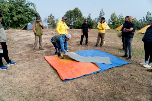 A group of people standing around a blue and orange blanket