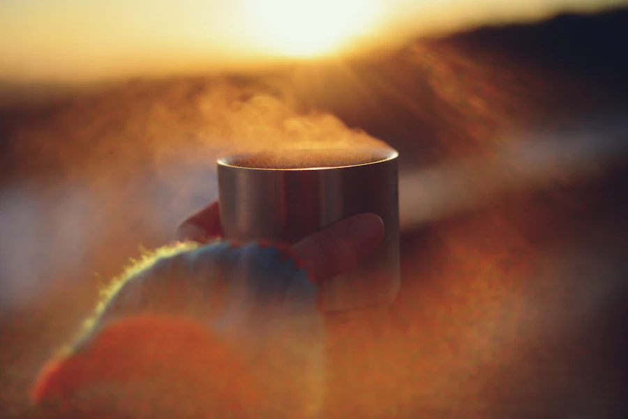 An adult's hand cradling a warm steaming mug at sunrise, close up in soft golden light