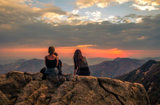 Two women sitting on top of a large rock