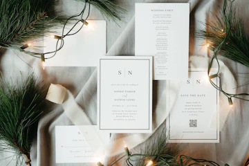 A Christmas-themed wedding stationery suite laid out on a table with fairy lights