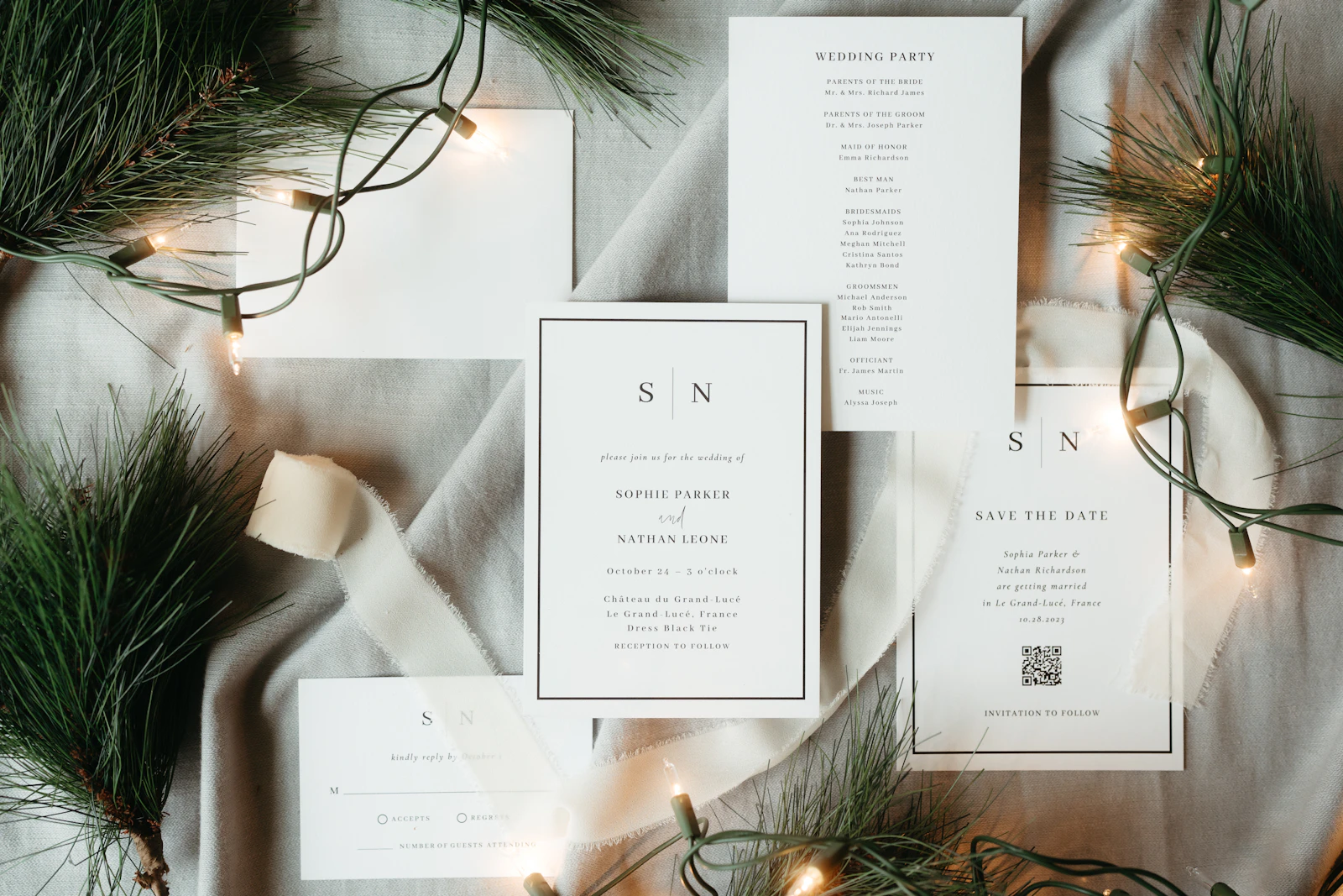 A Christmas-themed wedding stationery suite laid out on a table with fairy lights