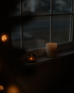 A candle sitting on a window sill next to a window
