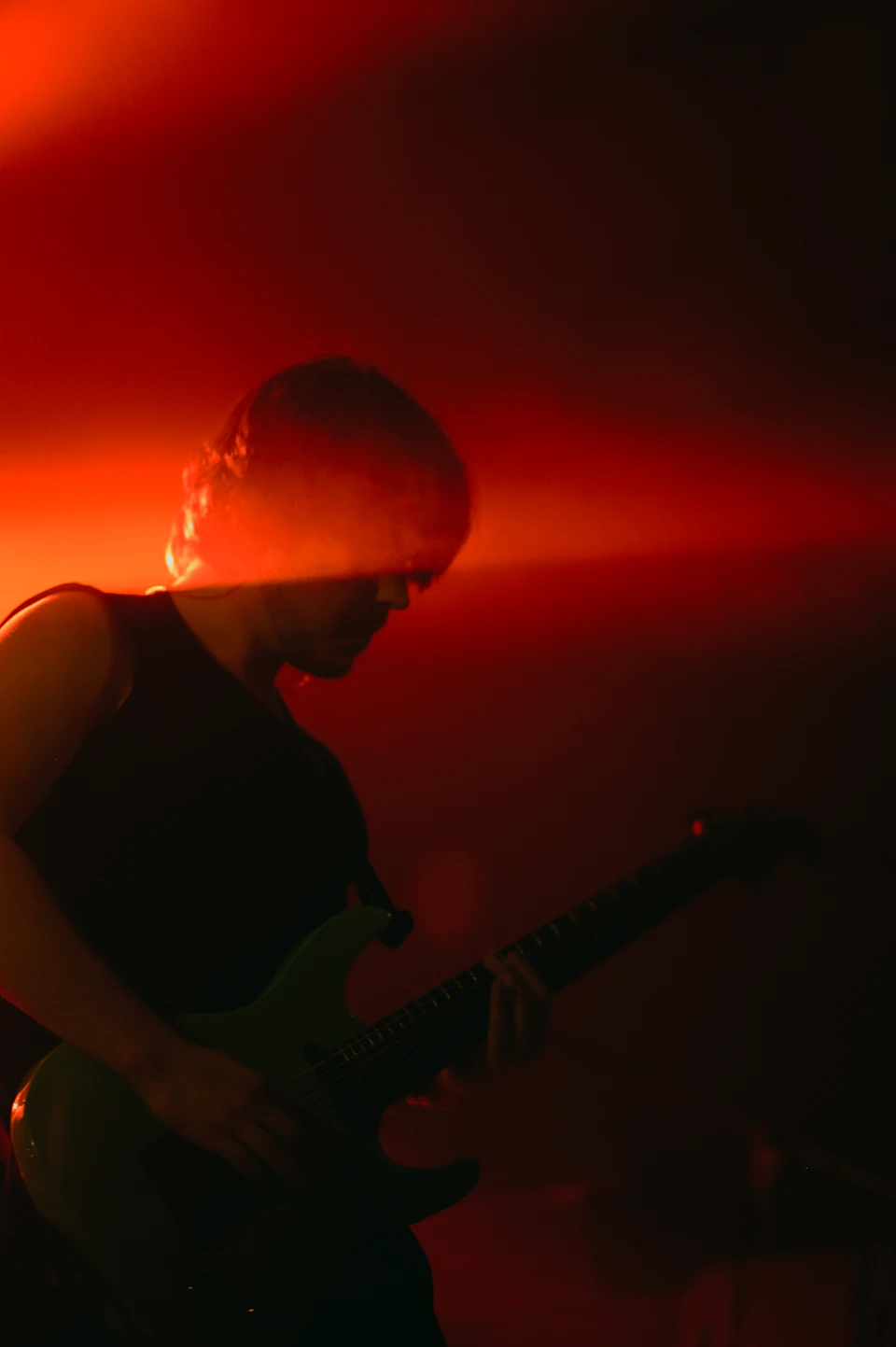 Person plays green electric guitar on stage under bright red spotlight