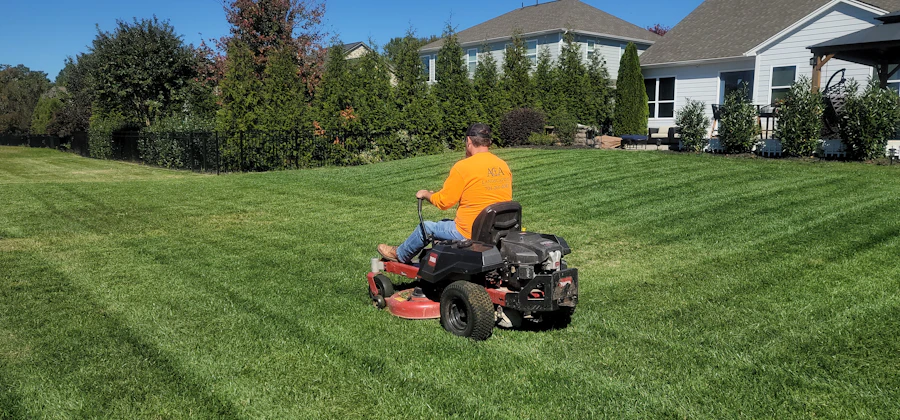Crew member riding a mower across a large lawn