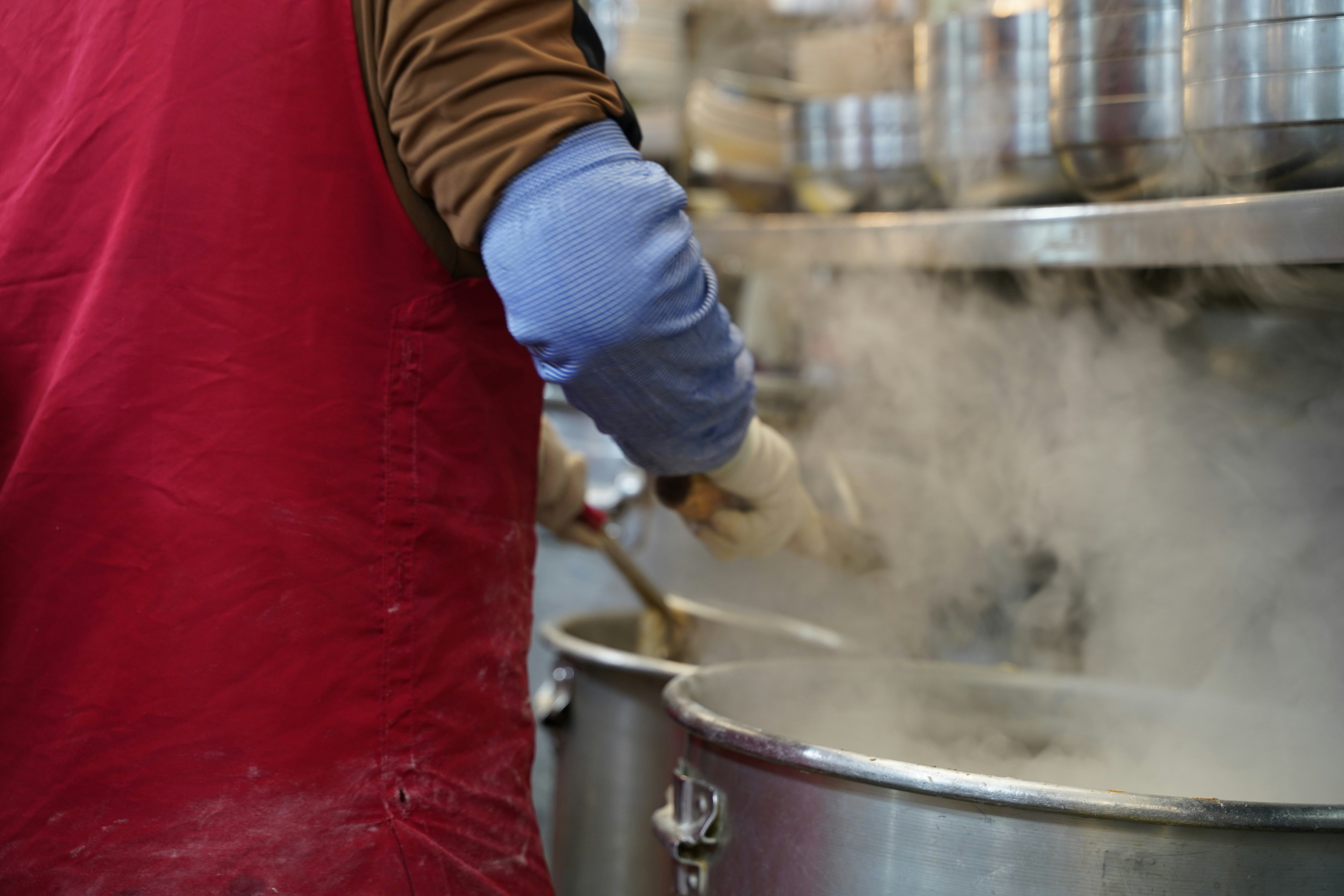 A man in a red apron stirring a pot of food