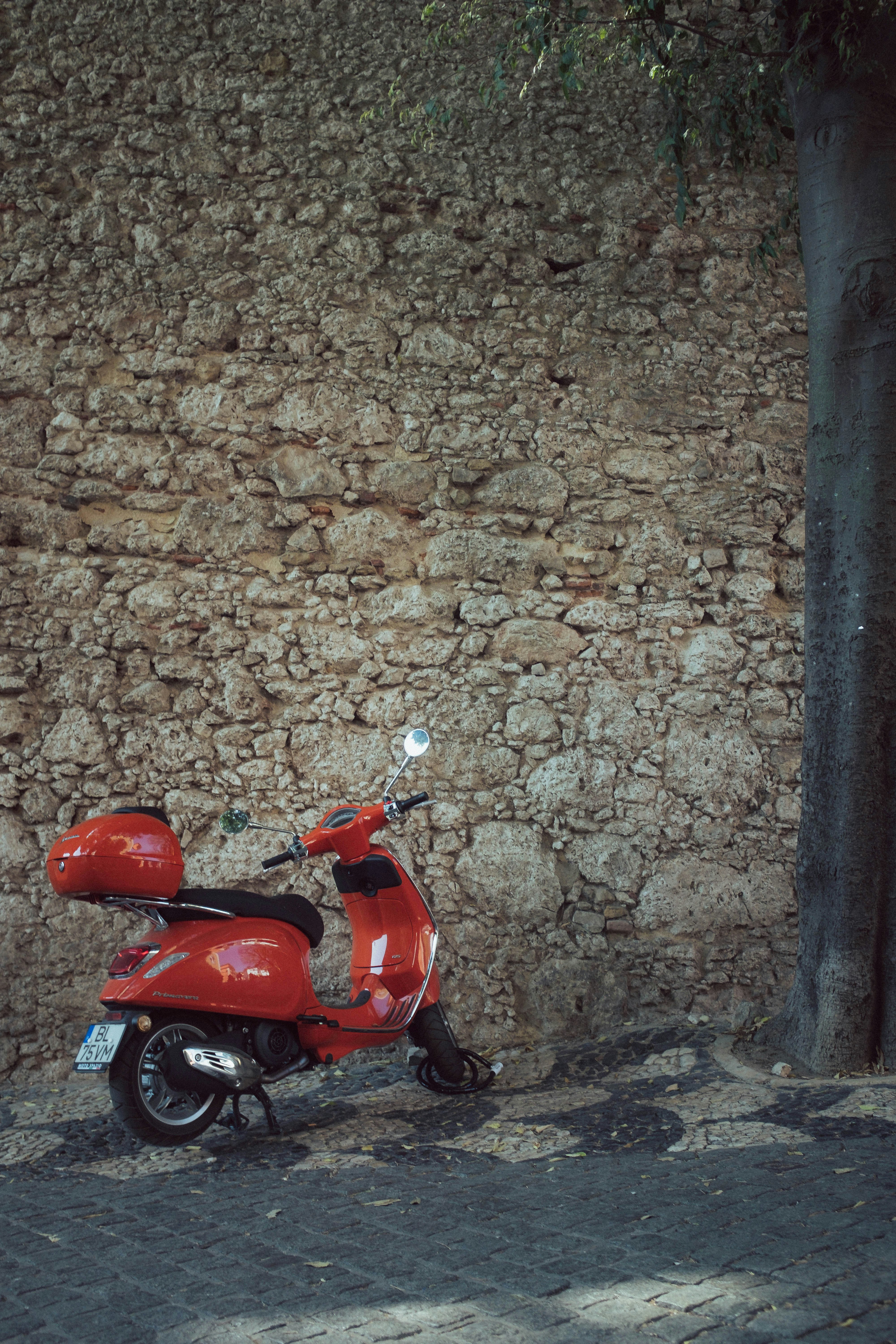 A red scooter parked in front of a stone wall