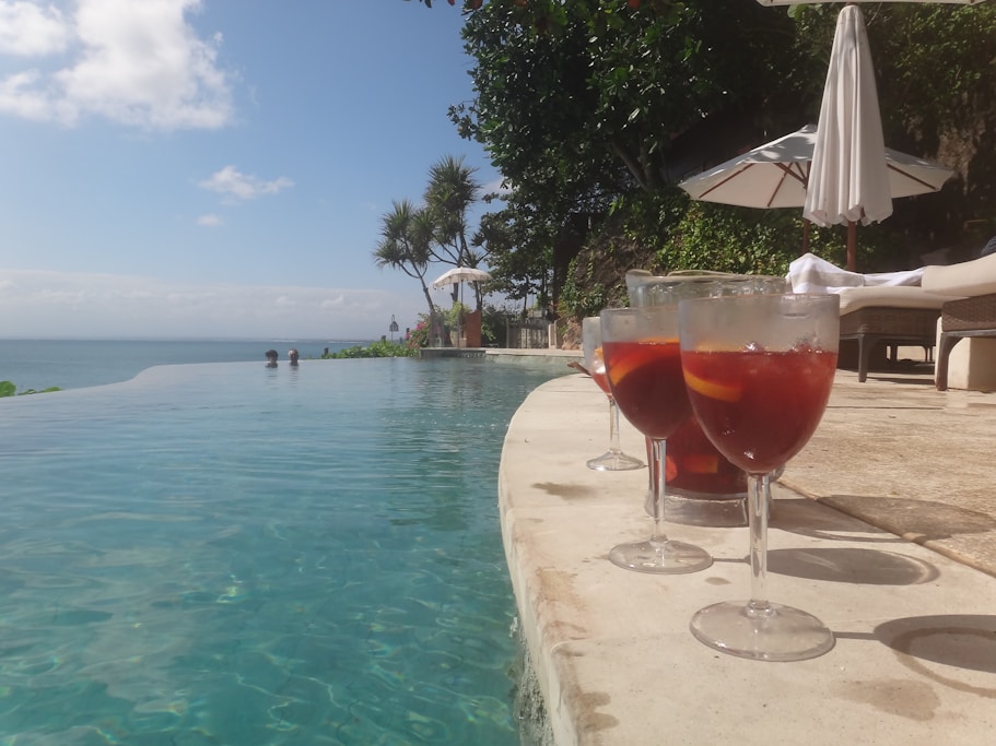 Two glasses of wine sitting next to a swimming pool