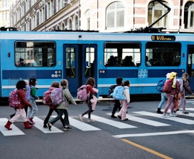 A group of people crossing a street in front of a blue train