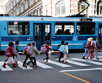 A group of people crossing a street in front of a blue train