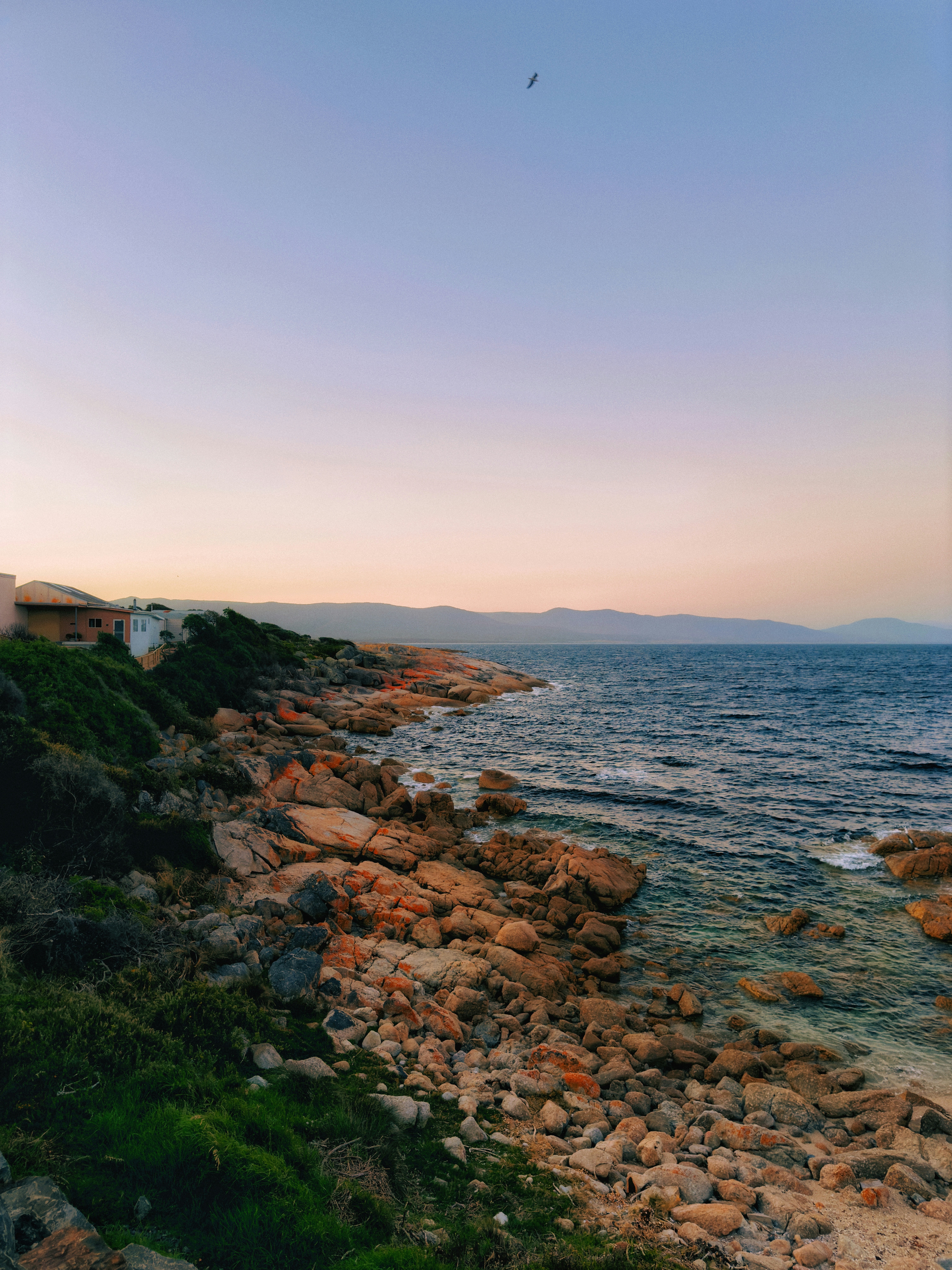A lighthouse on a rocky shore at sunset