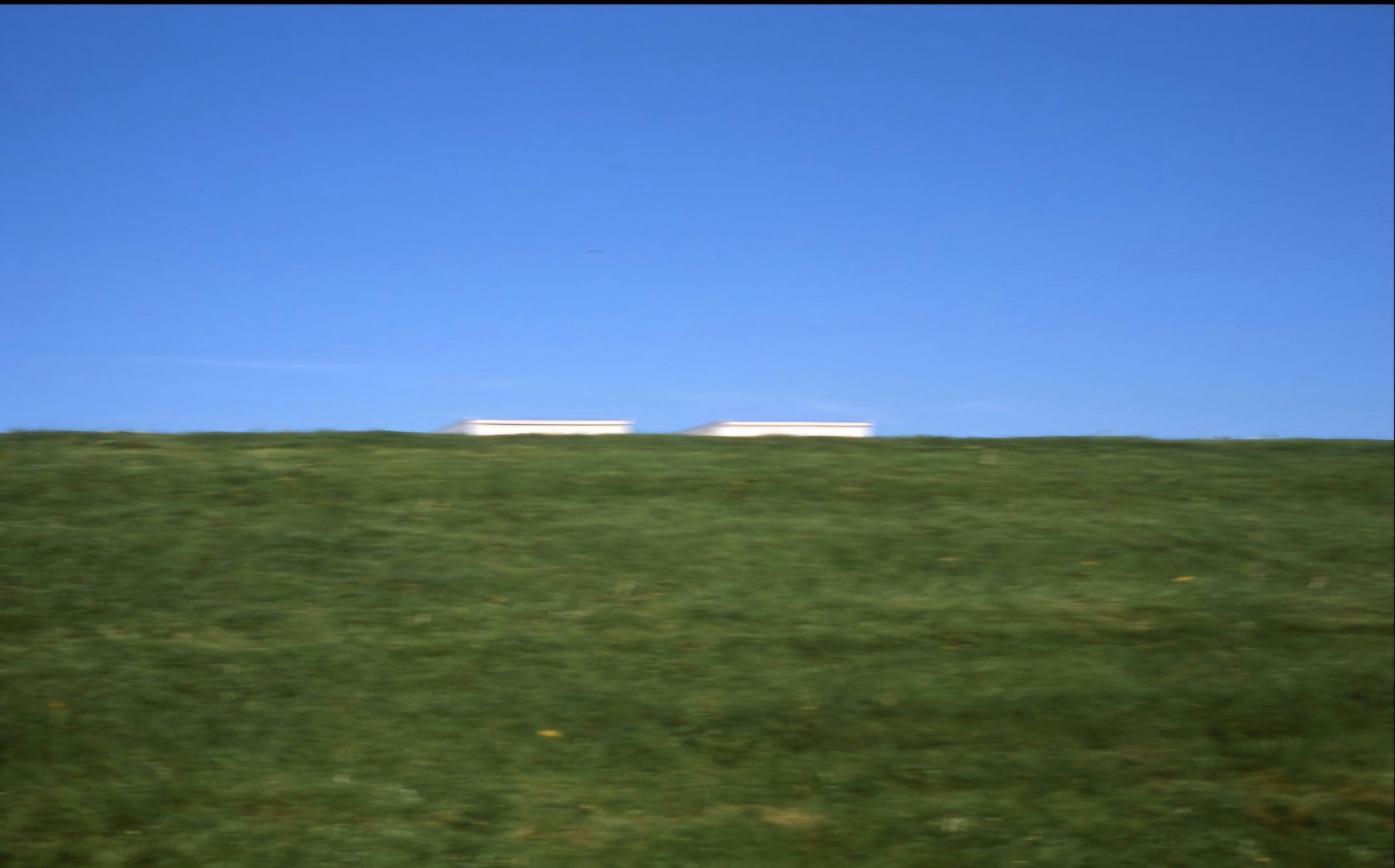 Ein grasbewachsenes Feld mit ein paar Heuballen in der Ferne