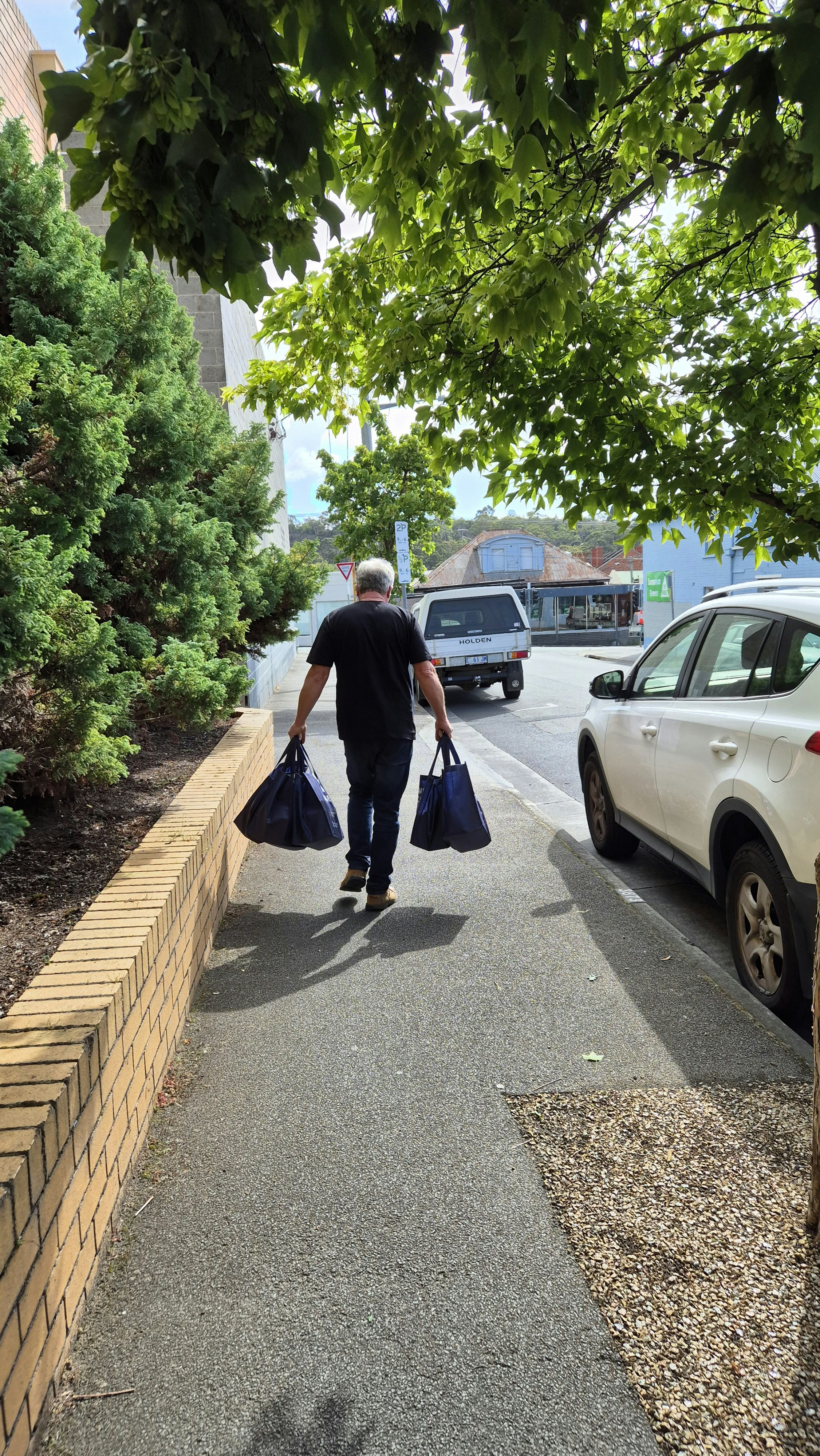 A man walking down a sidewalk carrying two bags