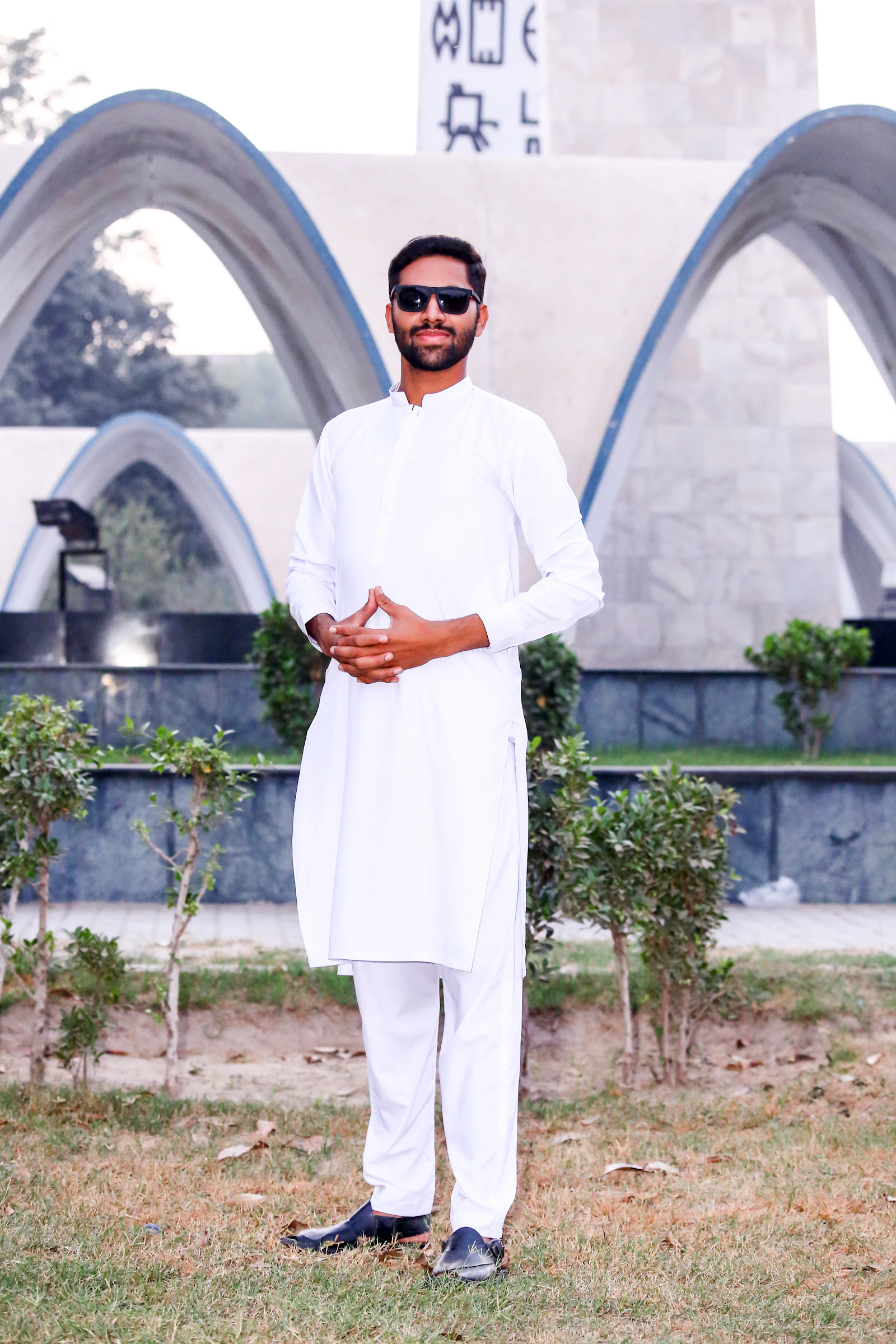 Man in white shalwar kameez standing, sunglasses